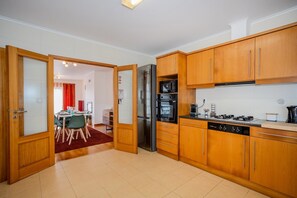 A modern kitchen with wooden cabinets, a refrigerator, oven, microwave, and a gas stove. - GuestReady - Casa Santa Maria (Ponta Delgada)