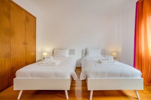 Een hotelkamer met twee eenpersoonsbedden, een houten garderobe en een feloranje gordijn.