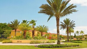 A yellow building with a sign reading "Bella Vida" surrounded by palm trees and well-maintained landscaping. - Cozy 3BR Townhome - Pool - Bella Vida Resort! (Kissimmee)
