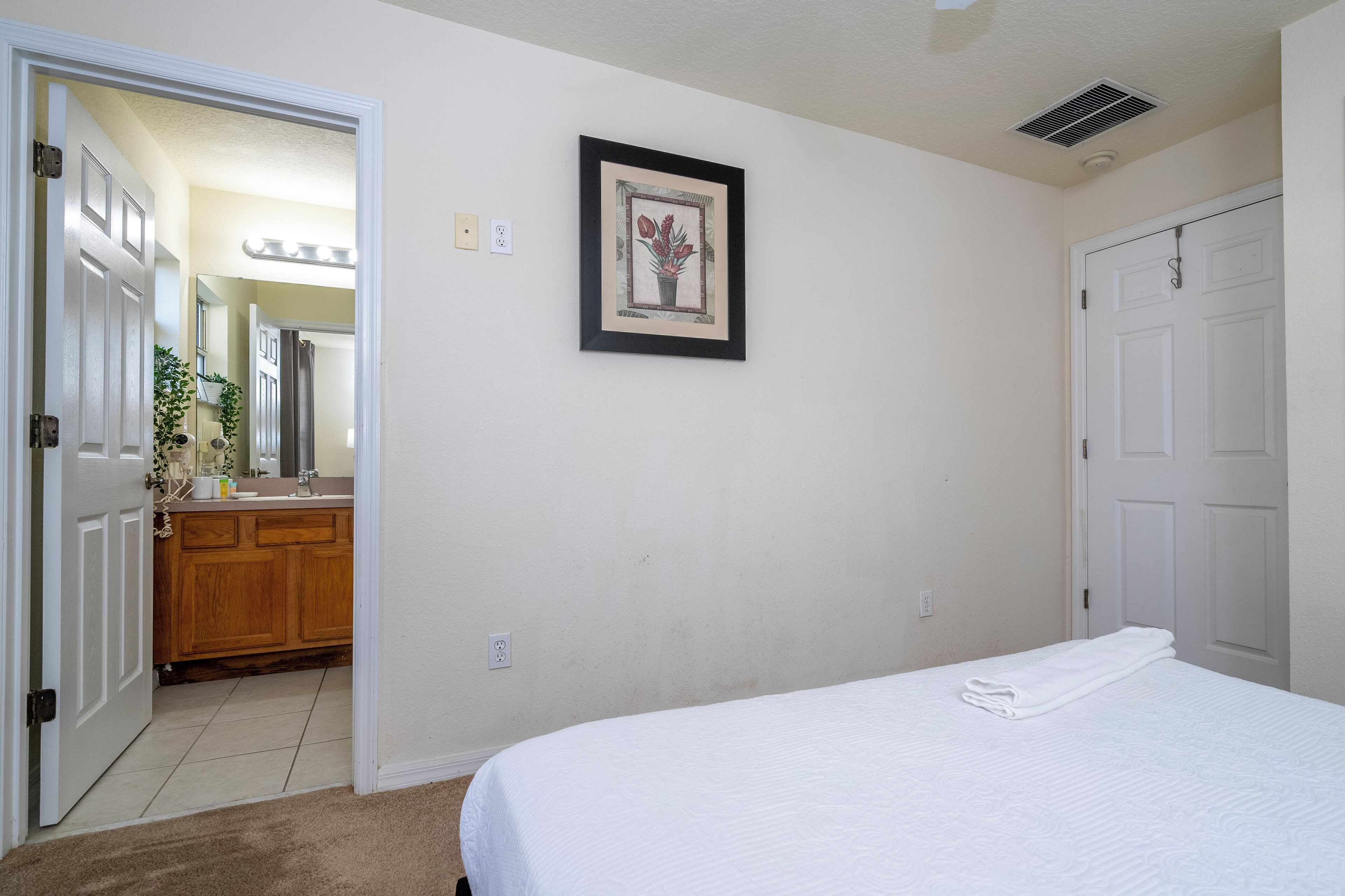 Een slaapkamer met een bed, een ingelijst schilderij aan de muur en een badkamer zichtbaar door een geopende deur.
