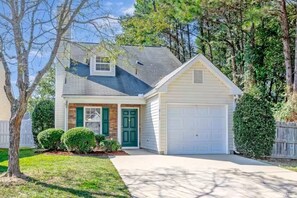 A single-story house with a garage, a front porch, and a well-maintained lawn. - Cozy Corner Cottage (Raleigh)
