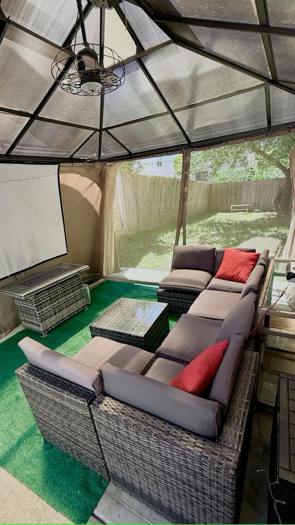 A covered outdoor seating area with wicker furniture and a view of a backyard.
