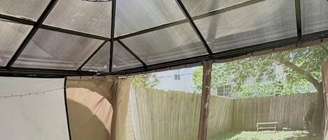 A covered outdoor seating area with wicker furniture and a view of a backyard.