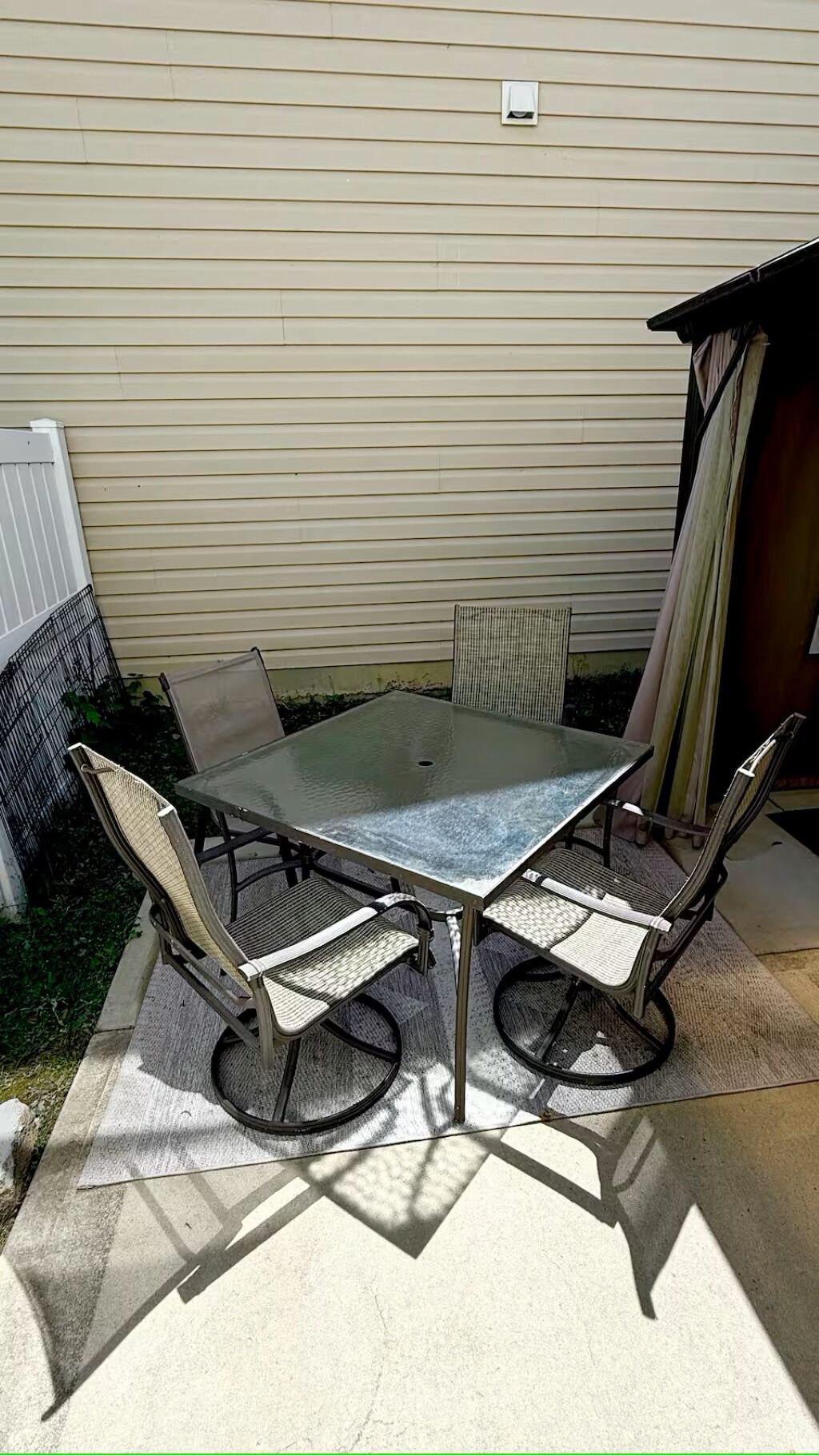 Ein Terrassentisch mit vier Stühlen, einem Metallgeländer und einer beige gestrichenen Außenwand.