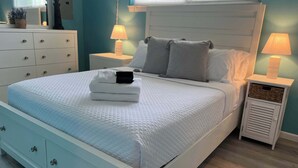 En pænt redt seng med et quiltet hvidt sengetæppe, et lille natbord med en lampe, og et sengebord med en lampe.