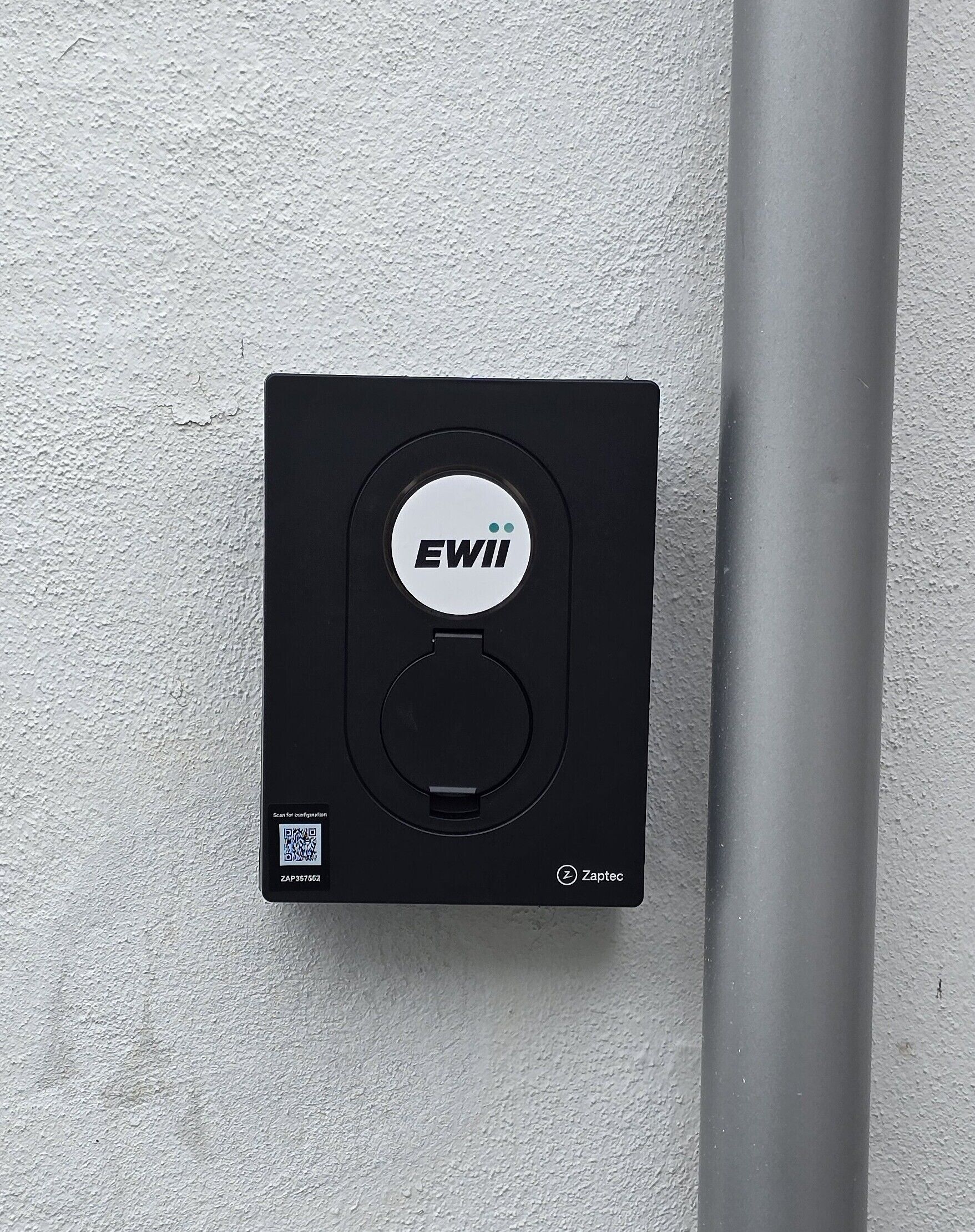Un dispositivo nero con il logo 'EWII', un codice QR e il marchio 'Zaptec' su un muro strutturato.
