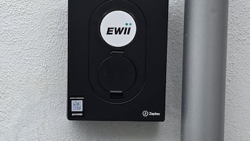 Un dispositivo nero con il logo 'EWII', un codice QR e il marchio 'Zaptec' su un muro strutturato.