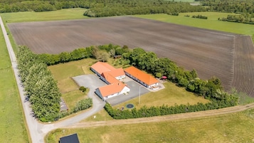 Vista aérea de una granja con dos edificios de techo rojo, un camino pavimentado y campos aledaños.