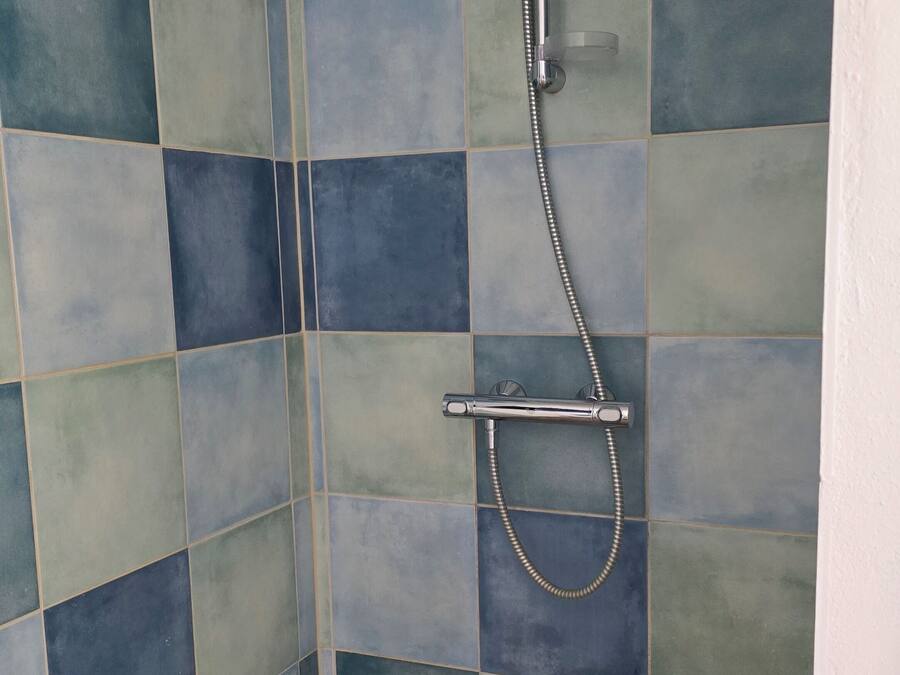 A shower area with a tiled wall and floor, a handheld showerhead, and a handheld shower attachment.