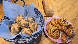 Un panier rempli de petits pains aux graines de pavot et une assiette de viennoiseries à la cannelle, posés sur une table en bois.