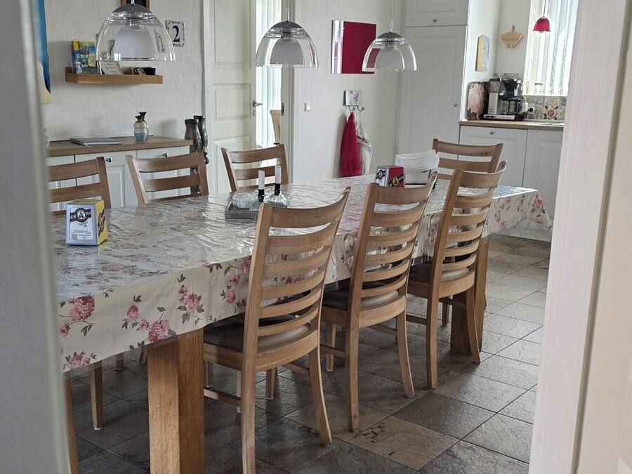 Comedor con una mesa dispuesta para cuatro personas, sillas de madera, suelo de baldosas y lámparas colgantes.