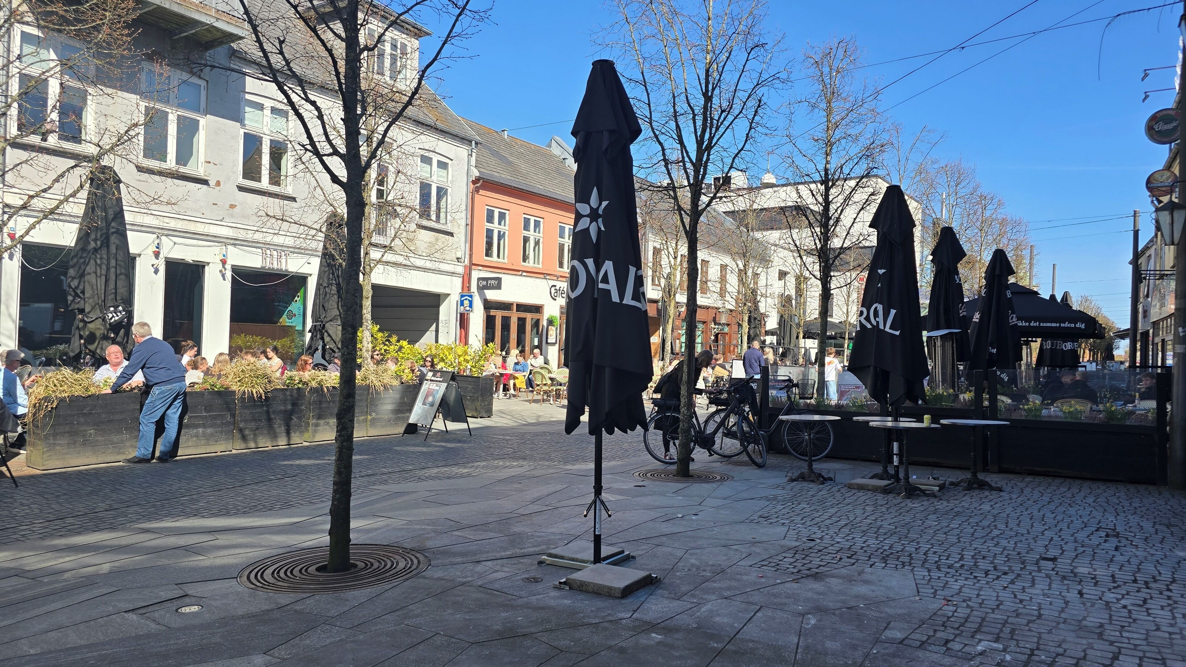 A cobblestone street with outdoor seating, a café, and a building with a sign that reads 'Café.'