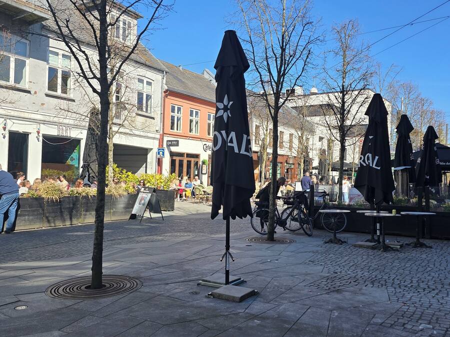 Eine Kopfsteinpflasterstraße mit Außenbestuhlung, ein Café und ein Gebäude mit der Aufschrift 'Café'.