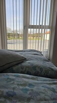 Una cama con ropa de cama estampada, una almohada y vista a través de una ventana con persianas verticales.