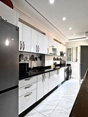 A modern kitchen with white cabinets, black countertops, and a built-in washing machine. - Modern 2BR Apartment with Pool & Parking – Near Beach in Tangier (Tangier)