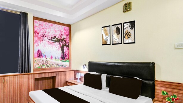 A hotel room with a bed, a nightstand, a lamp, a window with curtains, and wall art. - Deluxe Red Hills Lakdikapul Sitara Grand (Hyderabad)