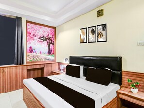 Une chambre d’hôtel comprenant un lit, une table de chevet, une lampe, une fenêtre avec des rideaux et des œuvres d’art murales.