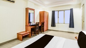 A hotel room with a bed, a desk with a chair, a wardrobe, a mirror, and a window with curtains. - Deluxe Red Hills Lakdikapul Sitara Grand (Hyderabad)