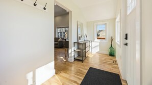 Un pasillo con suelo de madera, un perchero, un espejo, una consola y una puerta que da a otra habitación.
