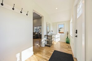 A hallway with wooden flooring, a coat rack, a mirror, a console table, and a door leading to another room.
