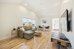 A modern living room with a sectional sofa, a coffee table, a wooden bench, and a TV mounted on the wall.