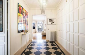Ein Korridor mit Schachbrettboden, einem Chandelier, einem Heizkörper und einer Tür mit weißem Feld.