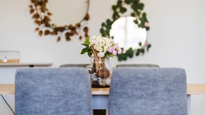 Une table à manger ornée d’un vase de fleurs, deux chaises grises et un miroir accroché au mur.