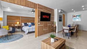 Een moderne woonkamer met een bed, een eethoek en een televisie waarop 'NETFLIX' wordt afgespeeld.