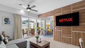 Een moderne woonkamer met een flatscreen televisie, een plafondventilator en een schuifpui naar een buitenruimte.