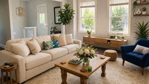 A living room with a beige sofa, a blue armchair, a wooden coffee table, and a large window with blinds. - Modern 3BR Apt 1st Fl Parking, WiFi, Laundry, Walk to 30+ Shops & Restaurants (Providence)
