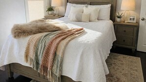 A bedroom with a bed, two bedside lamps, a painting above the bed, a nightstand with a lamp, a fluffy throw, and a rug. - Modern 3BR Apt 1st Fl Parking, WiFi, Laundry, Walk to 30+ Shops & Restaurants (Providence)