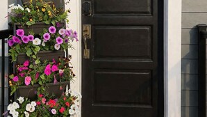 A dark front door with a wreath, a tiered flower planter, and a doormat. - Modern 3BR Apt 1st Fl Parking, WiFi, Laundry, Walk to 30+ Shops & Restaurants (Providence)