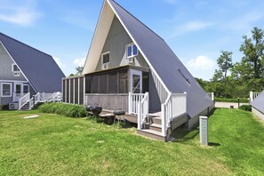 A modern house with a sloped roof, a porch with white railings, and a small outdoor seating area with a grill.