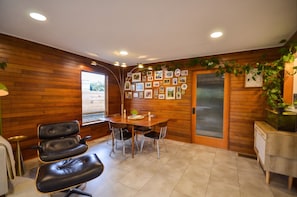 Ein Zimmer mit Holzwand, einem Esstisch mit Stühlen, einer kleinen Pflanze und gerahmten Bildern an der Wand.