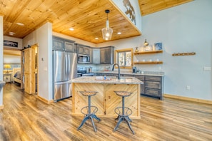 A spacious kitchen with wooden flooring, stainless steel appliances, and a central island with bar stools. - BaseCamp Bryson-Panoramic Views-Pet Friendly-Paved-Hot Tub-Fire-pit (Bryson City)