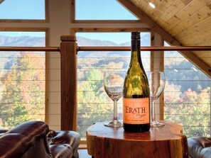 A bottle of Erath Pinot Noir on a wooden table with two glasses, in a room with a view of mountains through large windows. - BaseCamp Bryson-Panoramic Views-Pet Friendly-Paved-Hot Tub-Fire-pit (Bryson City)