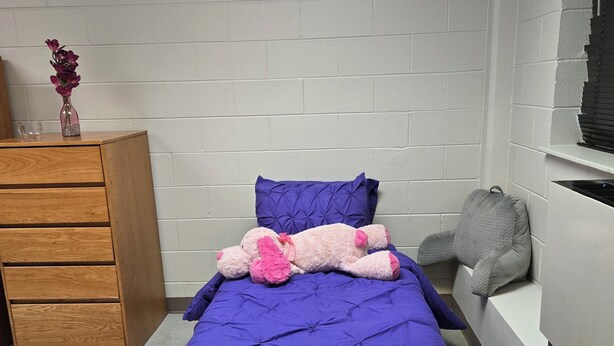 A bedroom with a single bed, a dresser, a window, and a wall-mounted heater.