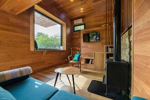 Una habitación acogedora con paredes de madera, un ventanal grande, chimenea, televisor y un espacio de estar cómodo.