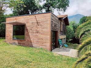 Una cabaña moderna de madera con un amplio ventanal, una terraza y vistas a las montañas.