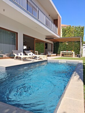 Un espace piscine moderne doté de chaises longues, d’un coin salon abrité et offrant une vue dégagée sur la piscine.