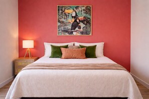 Une chambre à coucher avec un lit, des oreillers, une table de chevet, une lampe et un tableau au mur.