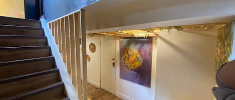 Una escalera conduce a una habitación con piso de madera, un cuadro en la pared y una silla amarilla.