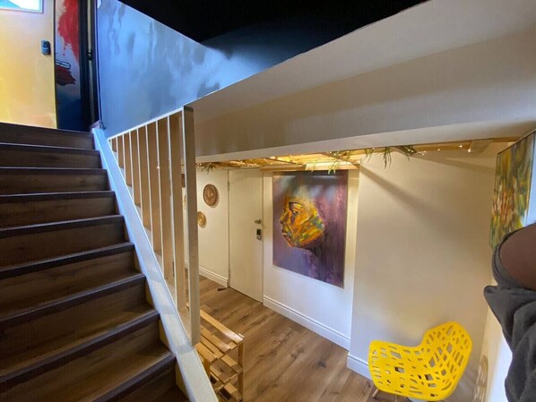 A staircase leading to a room with a wooden floor, a painting on the wall, and a yellow chair.