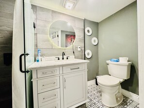 A bathroom with a white vanity, a round mirror, a toilet, and patterned floor tiles.