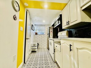 Une cuisine étroite avec des meubles blancs, un four à micro-ondes et une horloge au mur.