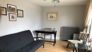A living room with a black sofa, a glass table, striped chairs, a radiator, and framed pictures on the wall.