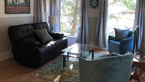 A living room with a black sofa, a blue armchair, a glass coffee table, and a wooden floor.