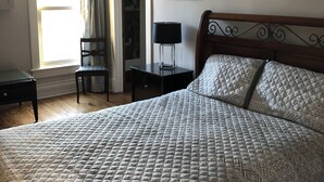 A bedroom with a bed, a chair, a nightstand, a lamp, a ceiling fan, and a framed picture on the wall.