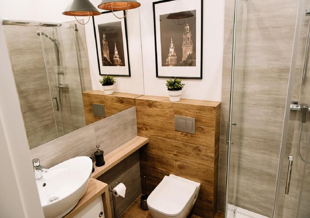 A modern bathroom with a glass shower enclosure, a wooden vanity, a sink, and two framed pictures on the wall.