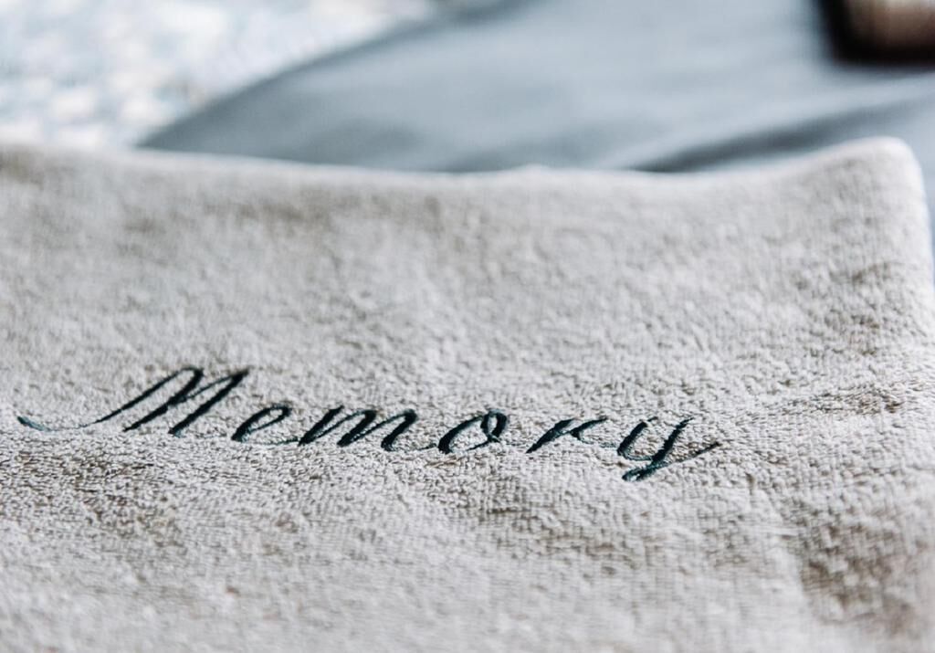A textured fabric with the word 'Memory' embroidered in cursive.